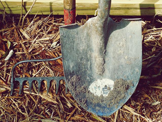 dreckige Schaufel und Gartenrechen im Stroh